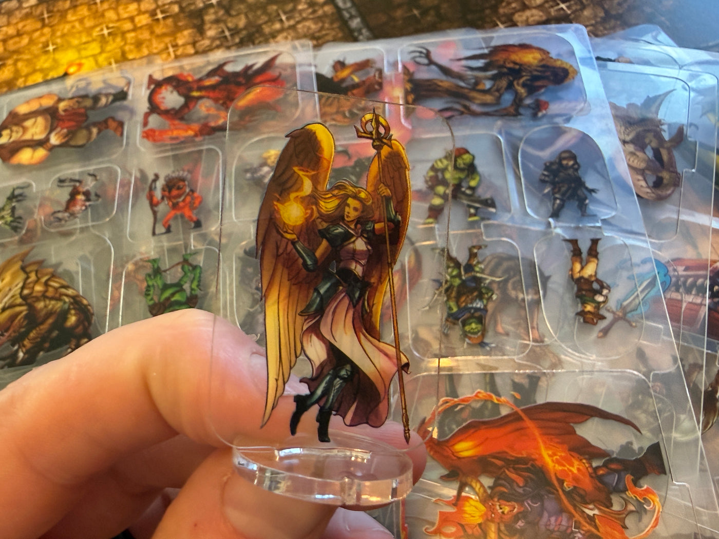 A winged Flat Plastic Miniature on its clear base, held in front of stacked flat miniature sheets